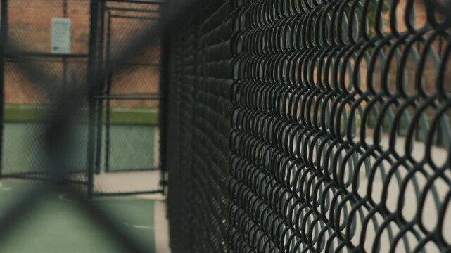 Slow glide follows a chain link court fence as blurred foreground fencing passes across frame.