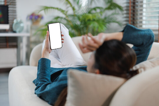 Woman relaxing on sofa holding phone with blank screen