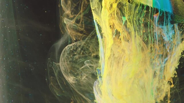 Dense yellow ink column pours from upper right into dark liquid, edged with turquoise and green ribbons and wrapped by pale translucent swirls and filamented tendrils