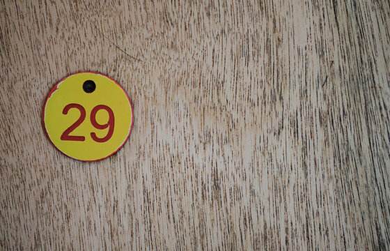 Yellow round tag with number 29 on light wood texture with copy space