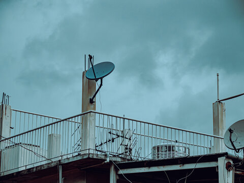 Rooftop Satellite Dish and Antennas Against Stormy Teal Sky, Urban Rooftop Scene
