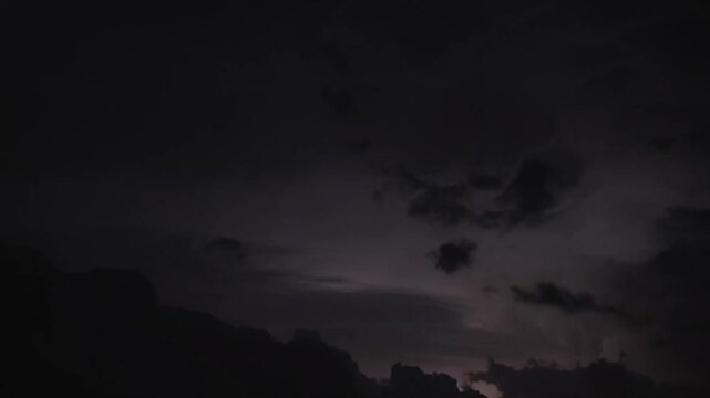 Intense continuous lightning flashes backlighting dramatic storm clouds over silhouetted hills