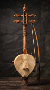 Traditional hand carved wooden rebab bowed string instrument with bow isolated on dark textured wall background indoor studio photography