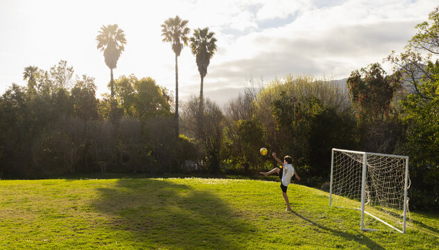 teenage boy playing with soccer ball in late afternoon light on field with palm trees in background