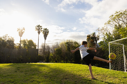 teenage boy playing with soccer ball in late afternoon light on field with palm trees in background