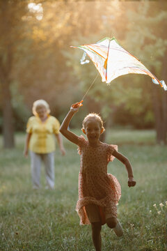 Granddaughter flying kite with grandmother in park at sunset