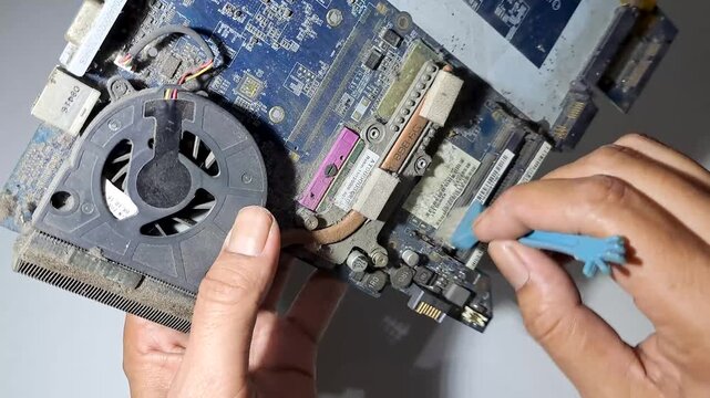 Close up of technician hands cleaning dusty laptop RAM slot on motherboard with a small brush during hardware maintenance and repair service.