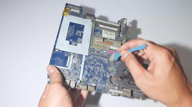 Technician hand cleaning dusty electronic microchips on laptop motherboard using brush tool concept of computer hardware repair service circuit board mainboard dust removal technical support