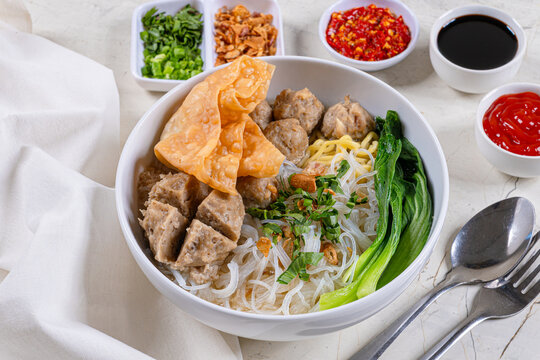 Authentic indonesian bakso meatball soup with noodles bok choy wonton and spicy condiments served on white marble restaurant table