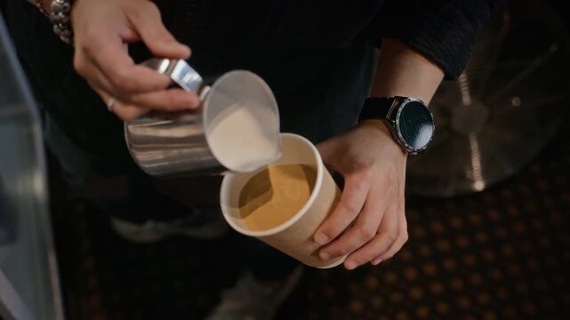 Barista pouring steamed milk from pitcher into paper cup making latte art from top view. Ideal for cafe advertising, beverage branding, and coffee shop marketing campaigns