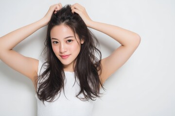 Fototapeta premium Young woman with long dark hair playfully touching her hair while smiling against a clean white background in an expressive casual pose. Generative AI