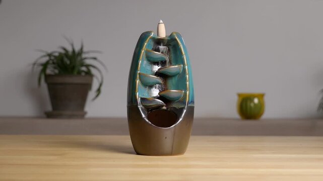 Incense burner with cascading smoke effect on wooden table for relaxation and meditation.