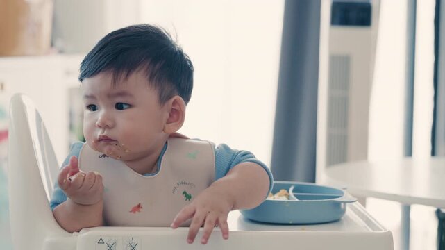 Asian baby boy self feeding sweet corn using baby led weaning method at home.	
