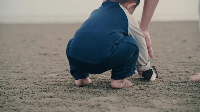 Low angle close up of toddler bare feet standing and stepping on sandy beach.