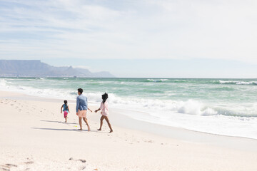 Obraz premium Full length of multiracial parents walking behind son on shore at beach during sunny day