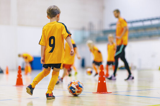 Junior Player in Yellow Number 9 Jersey Dribbling Ball Around Cones - Youth Indoor Futsal Training Practice Session in Sports Hall Gymnasium