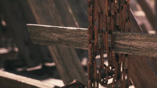 A close view of rusty chains hanging from aged wood. This setting suggests neglect and a past use, hinting at times effect on materials. The light casts shadows on the surfaces.