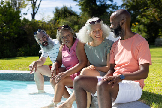 Diverse group of seniors sitting by pool, enjoying sunny day together