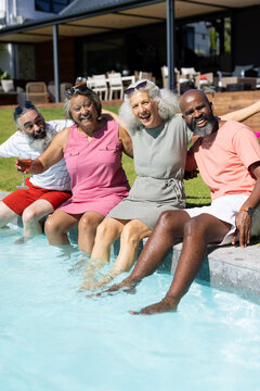 Diverse group of senior friends sitting by pool, enjoying summer day together