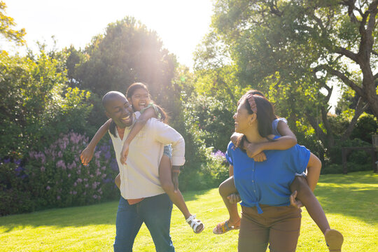 Playing in garden, multiracial parents giving piggyback rides to daughters, smiling and laughing