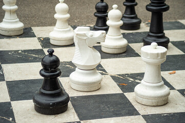 Large chess pieces stand on a giant outdoor pavement board in Switzerland. The strategic public game features oversized black and white figures including a prominent knight and rook. © dsbedarieva