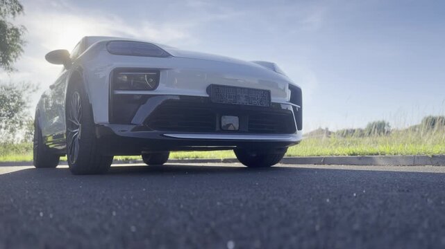 Low angle view of a white sports car parked on an empty road with sunlight and grassy countryside background