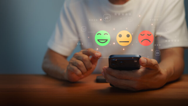 Man using smartphone to give online customer satisfaction feedback. Futuristic digital hologram shows happy, neutral, and sad face rating icons for business service review survey.