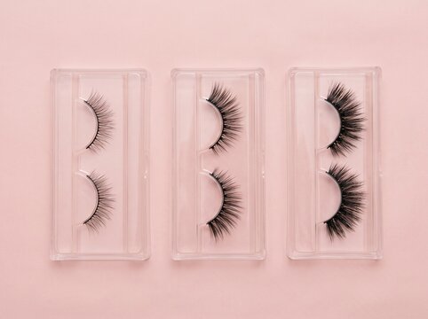 Flat lay of three different false eyelash pairs in clear plastic trays on soft pink background, symbolizing beauty cosmetics variety
