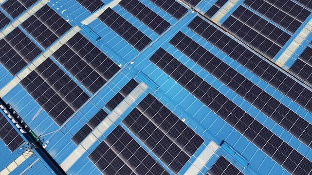 Large-scale rooftop solar panel array viewed from above, rows of photovoltaic modules installed on a blue industrial roof generating renewable clean energy
