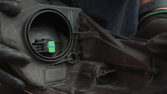 Automotive mechanic wearing gloves unplugging the electrical connector on the back of a car headlight
