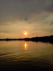 Obraz premium Breathtaking golden sunset reflecting on calm lake water with distant shoreline silhouette