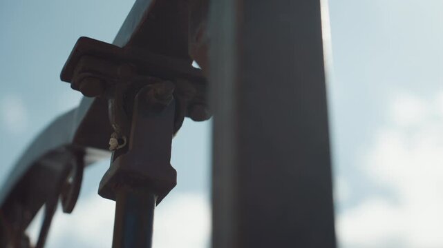 Close up of metal bracket with bolts and rusted details showing structural components in focus against out of focus sky background. scene highlights texture detail on industrial hardware