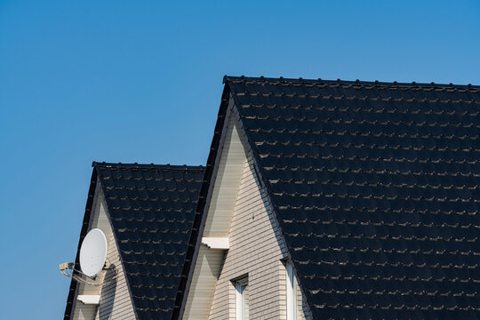 Blue sky over two houses with black roofs and satellite dish