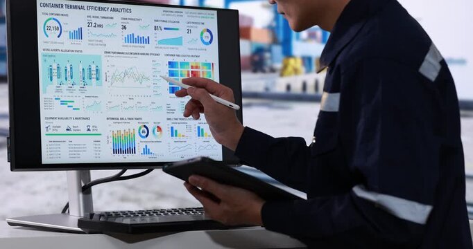 Industrial worker using a tablet beside a monitor energy efficiency charts and factory data in a modern control room.