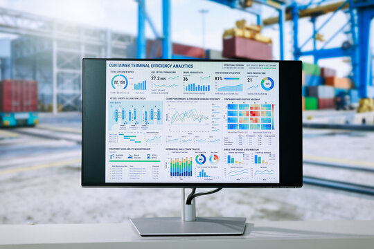 Computer monitor a container terminal analytics dashboard at a cargo port, with cranes, stacked shipping containers and rail tracks blurred in the background.