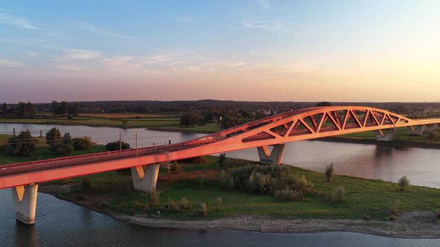 A yellow and blue intercity passenger train of the Nederlandse Spoorwegen NS travels over the Hanzeboog Railway bridge during a summer sunset in Overijssel, Netherlands.