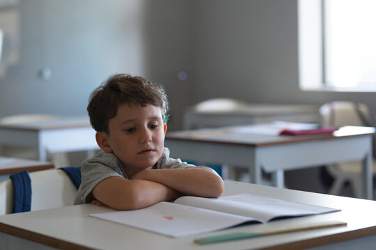 Young boy in school classroom reading book, looking thoughtful and focused, copy space
