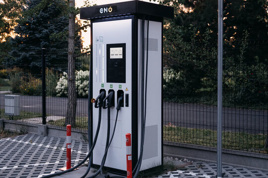 Electric vehicle charger with idle screen, RFID reader and three connectors stands empty beside fence at sunset. Charging infrastructure shortage, EV adoption barrier, Warsaw, Poland, 20 July 2026