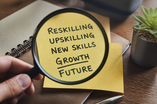 A hand holds a magnifying glass over words like RESKILLING and FUTURE on paper on a wooden desk.