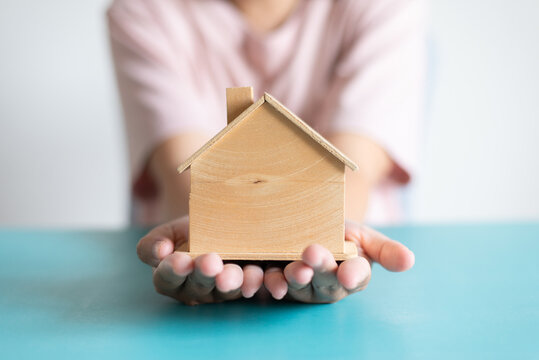 Hands holding wooden house model on blue table