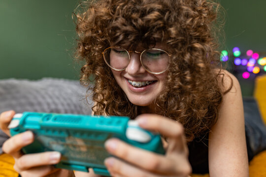 Smiling teenage girl plays a handheld video game console indoors