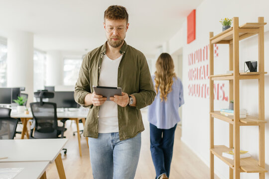 Mid adult man reads on digital tablet while walking in modern office