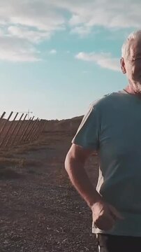 Active senior man with white hair running on a gravel path in the countryside, enjoying a healthy lifestyle and outdoor fitness routine during a sunny day with a blue sky in the background