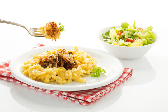 Plate of spaetzle with cheese and roasted onions besides salad bowl, close up