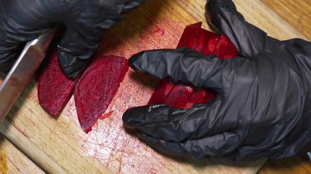 Chef slicing fresh beet into thin pieces on a wooden board. Top down close-up shot.