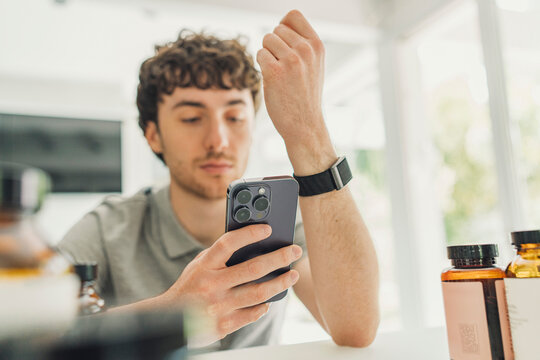 Male checking health tracker on phone with supplements indoors