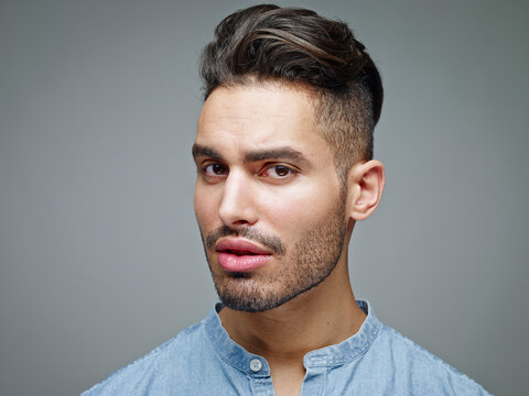 Portrait of sceptical looking young man in front of grey background