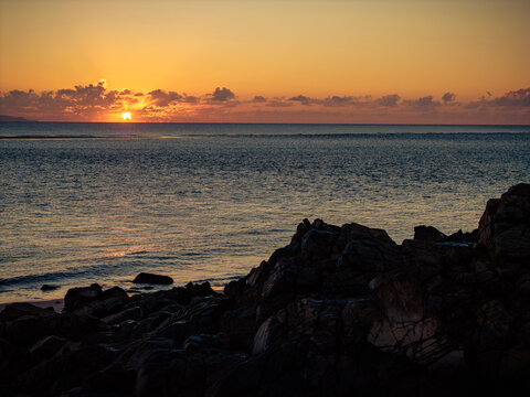 Aerial video along a tropical beach at dawn with golden sunrise over rocks Mackay Queensland Australia