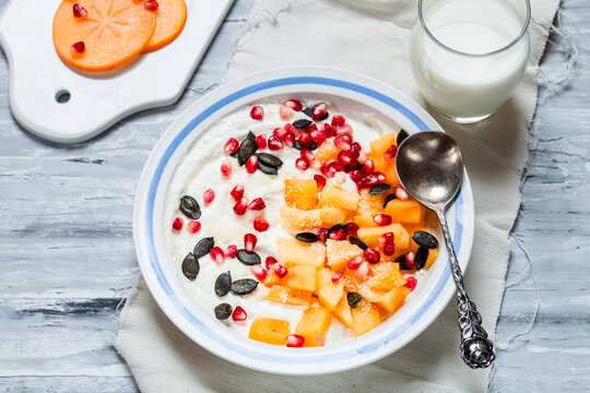 Dish of natural yoghurt, kaki, pomegranate seed, almond and pumpkin seed