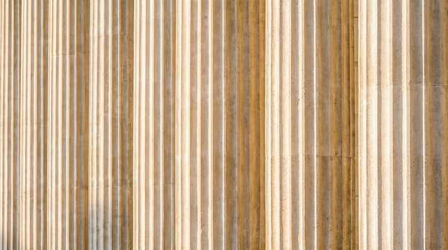 Close up perspective showing repetitive beige fluted stone pillars standing perfectly straight creating classical architectural patterns under warm afternoon sunlight